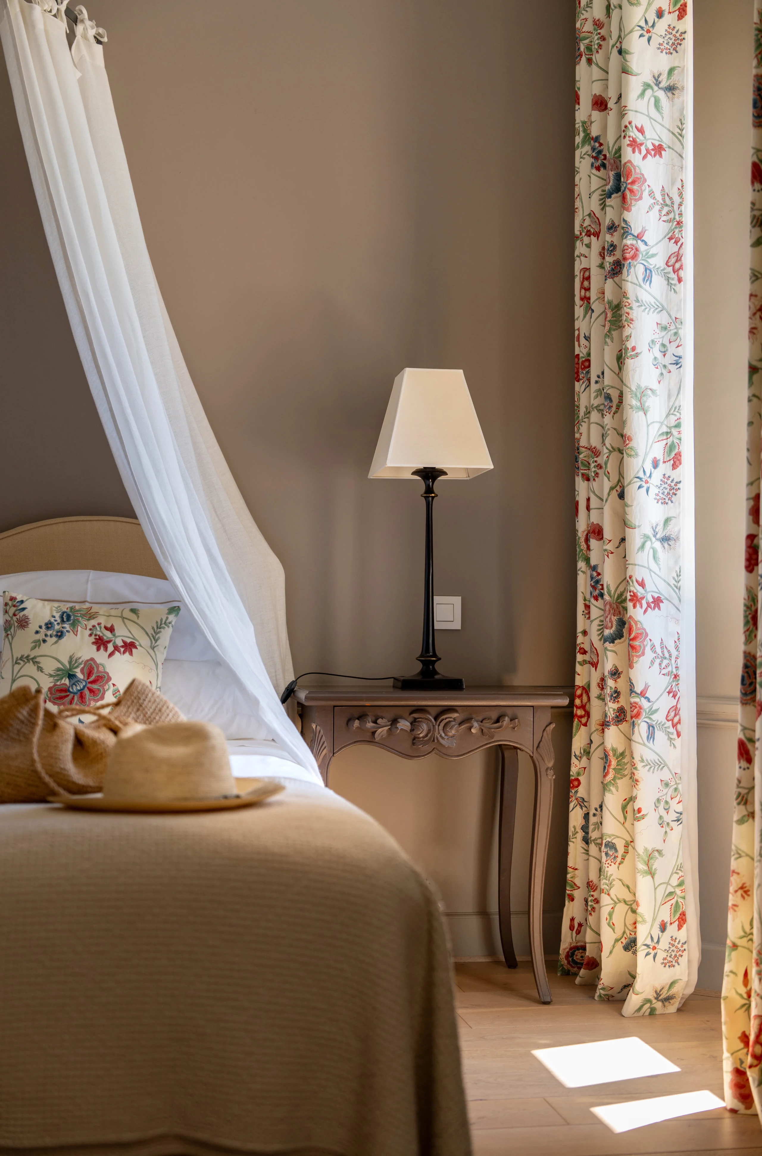 Chambre avec lit, lampe, rideaux fleuris.